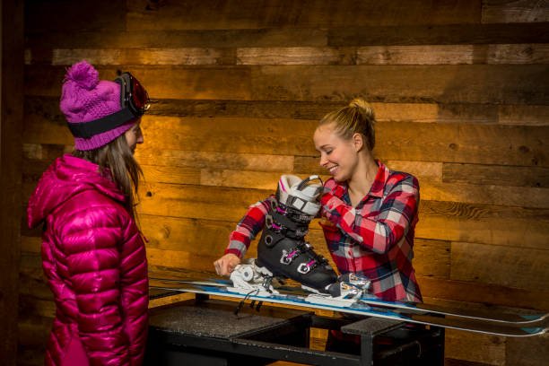 Twee vrouwen stellen een skischoen af op een ski tegen een houten wand